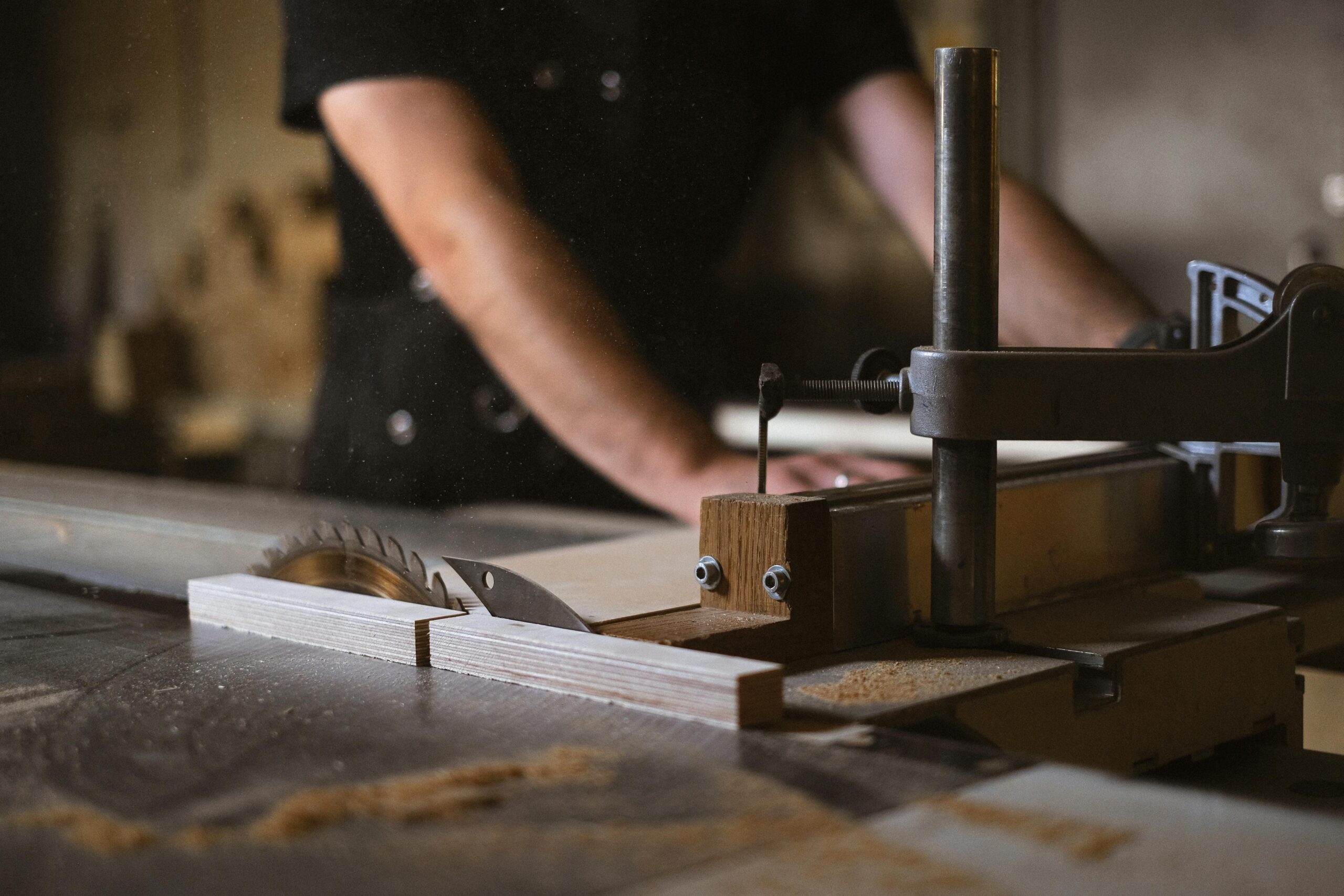 Unrecognizable blurred male carpenter cutting wooden details at sawbench with sharp knives while working in professional joinery with special instruments